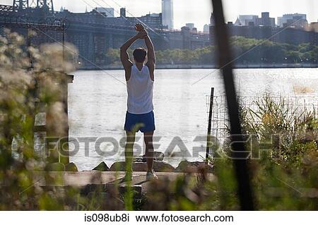 Stock Image - Male runner stretching by river. Fotosearch
