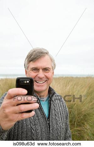 Stock Image - Man at the coast with camera phone. Fotosearch