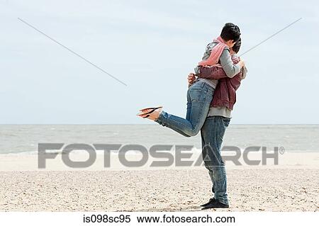 Stock Photography - Man by the sea lifting up girlfriend. Fotosearch