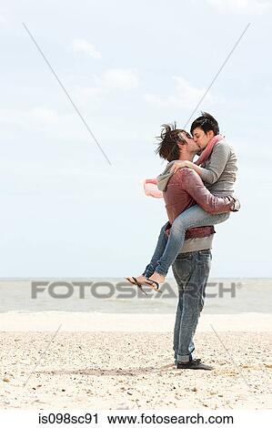 Stock Image - Man carrying girlfriend by the sea. Fotosearch
