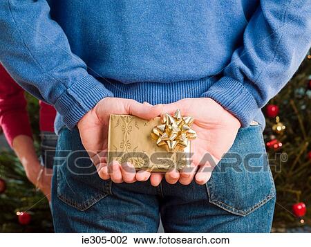 Man hiding a christmas present behind back View Large Photo Image Stock Image - Man hiding a christmas present behind back. Fotosearch