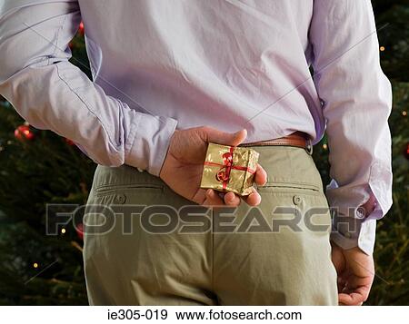 Man hiding a christmas present behind back View Large Photo Image Stock Photo - Man hiding a christmas present behind back. Fotosearch