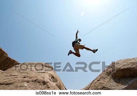 Stock Image - Man leaping between large boulders. Fotosearch