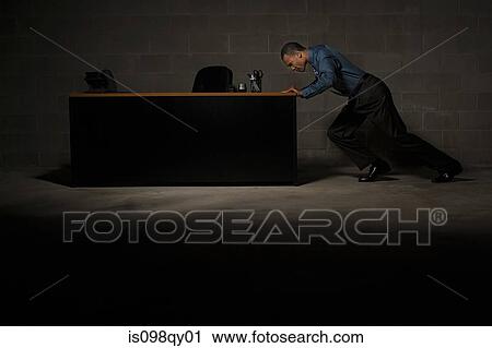 Stock Image - Man pushing desk. Fotosearch