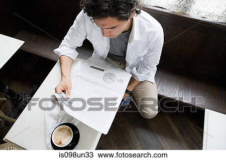 Stock Image - Man reading newspaper in coffee shop. Fotosearch