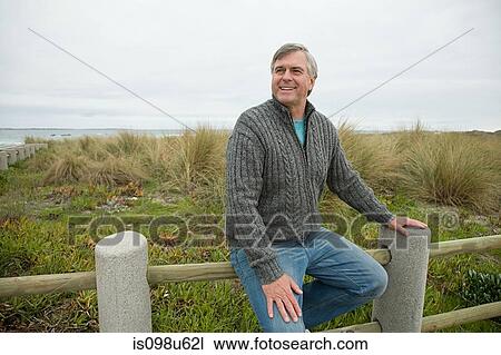 Man sitting on a fence at the coast View Large Photo Image Stock Image - Man sitting on a fence at the coast. Fotosearch