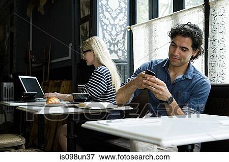 Stock Photo - Man with cellphone and woman with laptop in cafe. Fotosearch