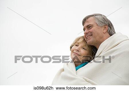 Stock Image - Mature couple outdoors, wrapped in blanket. Fotosearch