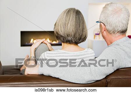 Stock Image - Mature couple sat next to the fire. Fotosearch
