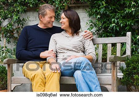 Stock Image - Mature woman and senior man sat on a bench. Fotosearch