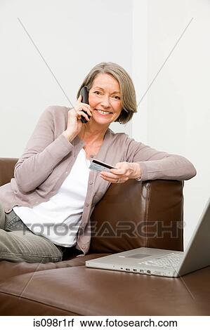 Stock Image - Mature woman using telephone banking. Fotosearch