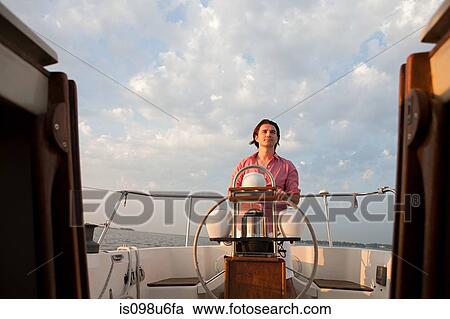 Stock Image - Mid adult man steering yacht. Fotosearch