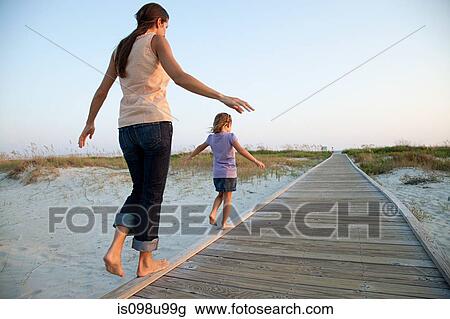 Stock Image - Mother and daughter walking on beach walkway. Fotosearch