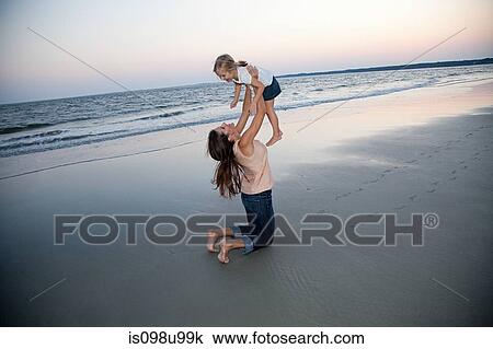 Mother lifting daughter on beach View Large Photo Image Stock Image - Mother lifting daughter on beach. Fotosearch