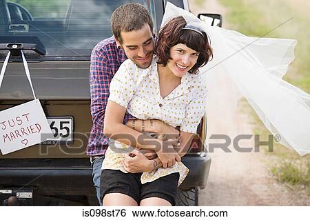 Stock Photograph - Newlywed couple by vehicle. Fotosearch