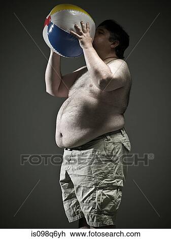 Stock Image - Overweight man blowing up beach ball. Fotosearch
