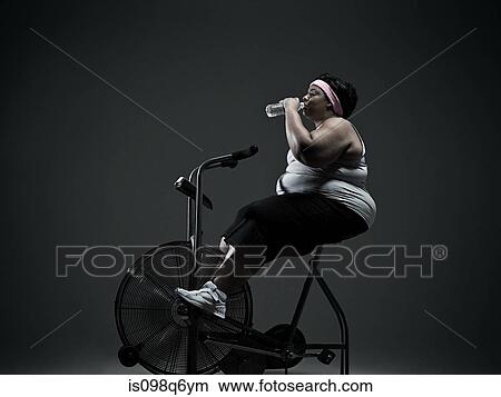 Picture - Overweight woman on exercise bike. Fotosearch