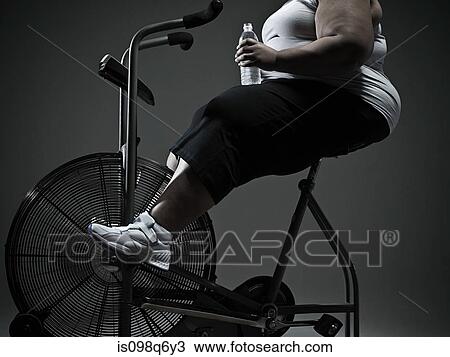 Stock Image - Overweight woman on exercise bike. Fotosearch