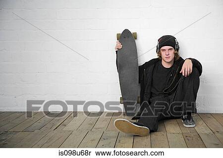 Stock Photography - Portrait of teenage boy sitting on floor with skateboard. Fotosearch