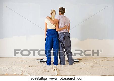 Stock Image - Rear view of couple looking at paint on wall. Fotosearch