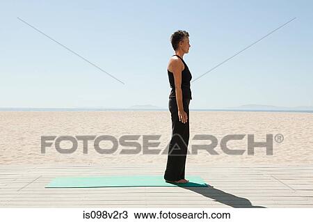 Stock Image - Senior woman doing yoga on beach. Fotosearch
