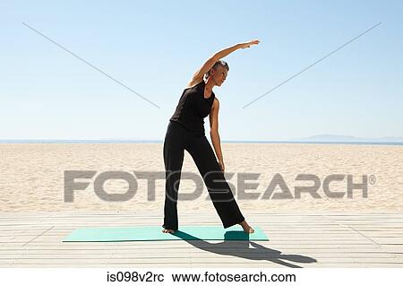 Stock Image - Senior woman doing yoga on beach. Fotosearch