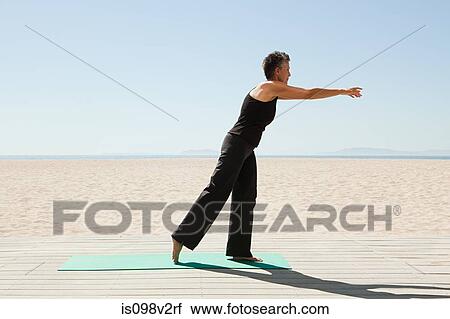 Stock Image - Senior woman doing yoga on beach. Fotosearch