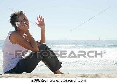 Stock Image - Senior woman using cell phone on beach. Fotosearch
