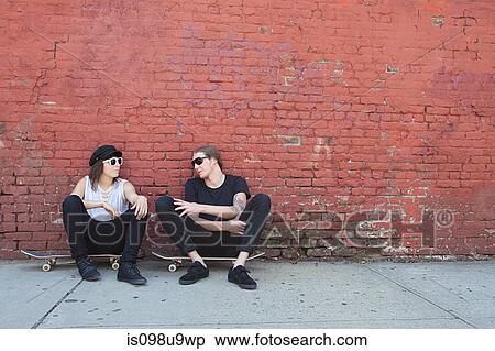 Stock Photography - Skaters sitting on boards by wall. Fotosearch