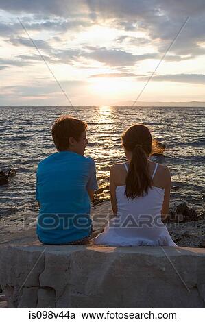Stock Image - Teenage couple watching sunset over sea. Fotosearch
