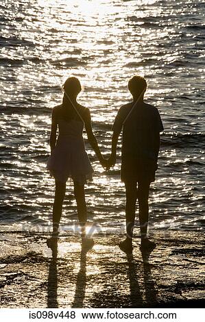 Stock Photo - Teenage couple watching sunset over sea. Fotosearch