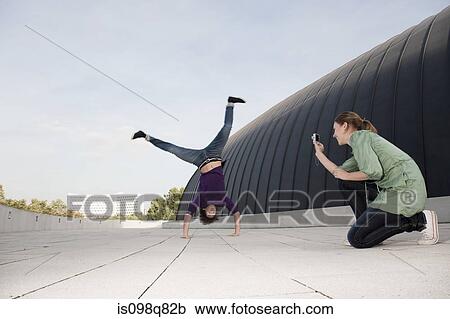 Teenage girl photographing young man doing a handstand View Large Photo Image Stock Image - Teenage girl photographing young man doing a handstand. Fotosearch