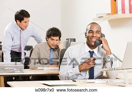 Stock Image - Three male office workers at their desks. Fotosearch