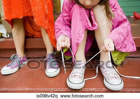 Two girls, one tying up shoelace View Large Photo Image Stock Photography - Two girls, one tying up shoelace. Fotosearch