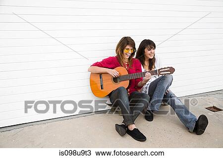 Stock Image - Two girls sitting on floor with guitar. Fotosearch