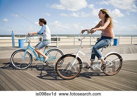 Stock Image - Two women cycling on boardwalk. Fotosearch
