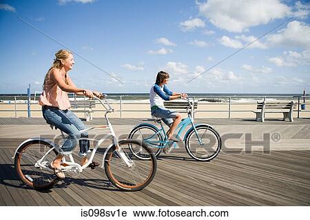 Two women cycling on boardwalk View Large Photo Image Stock Image - Two women cycling on boardwalk. Fotosearch
