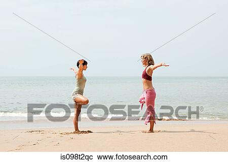 Two women practicing yoga on a beach View Large Photo Image Stock Image - Two women practicing yoga on a beach. Fotosearch