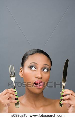 Stock Image - Uncertain looking woman holding cutlery. Fotosearch