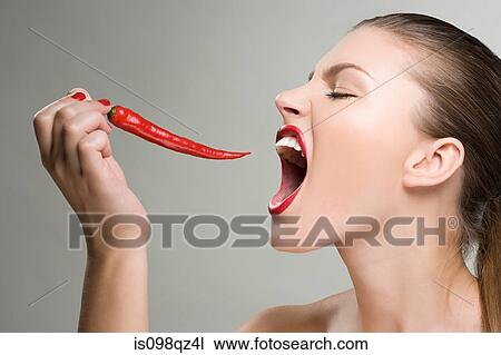 Stock Image - Woman biting a red chili pepper. Fotosearch