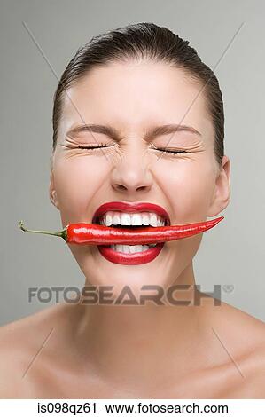 Stock Image - Woman biting a red chili pepper. Fotosearch
