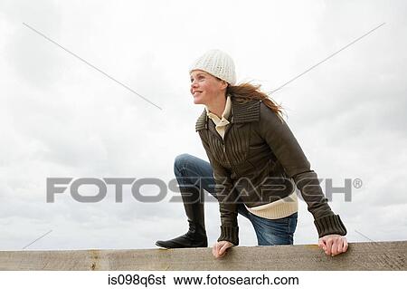 Stock Photograph - Woman climbing over wall. Fotosearch
