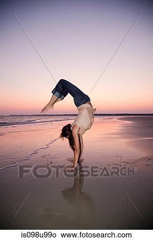 Picture - Woman doing a handstand on beach at sunset. Fotosearch