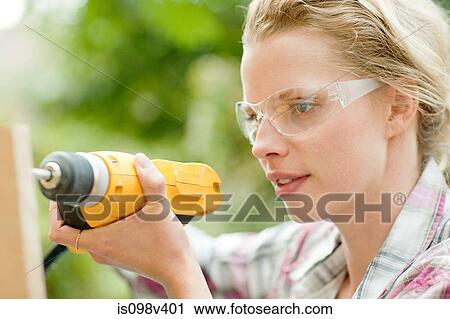 Stock Image - Woman drilling with electric drill. Fotosearch