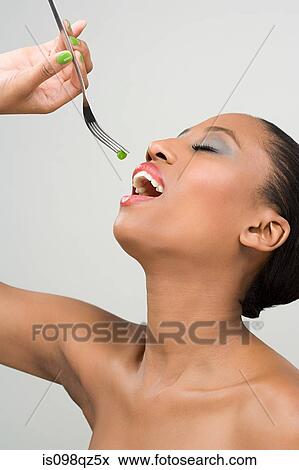 Stock Photo - Woman eating a pea on a fork. Fotosearch