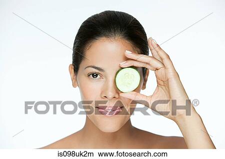 Picture - Woman holding cucumber over eye. Fotosearch