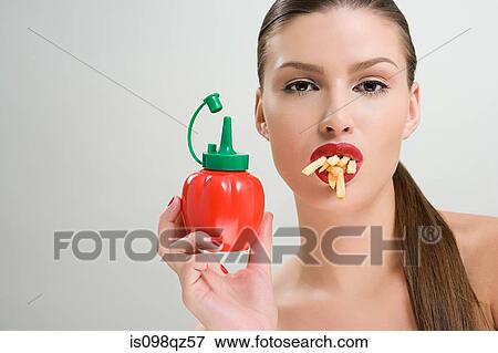 Stock Photo - Woman holding tomato ketchup and eating fries. Fotosearch