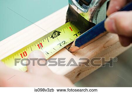 Stock Image - Woman measuring plank of wood and marking with pencil. Fotosearch