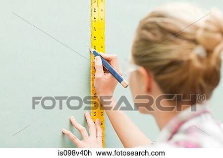 Stock Image - Woman measuring plywood and marking with pencil. Fotosearch
