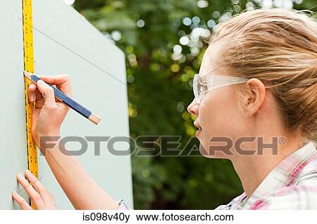 Stock Photo - Woman measuring plywood and marking with pencil. Fotosearch